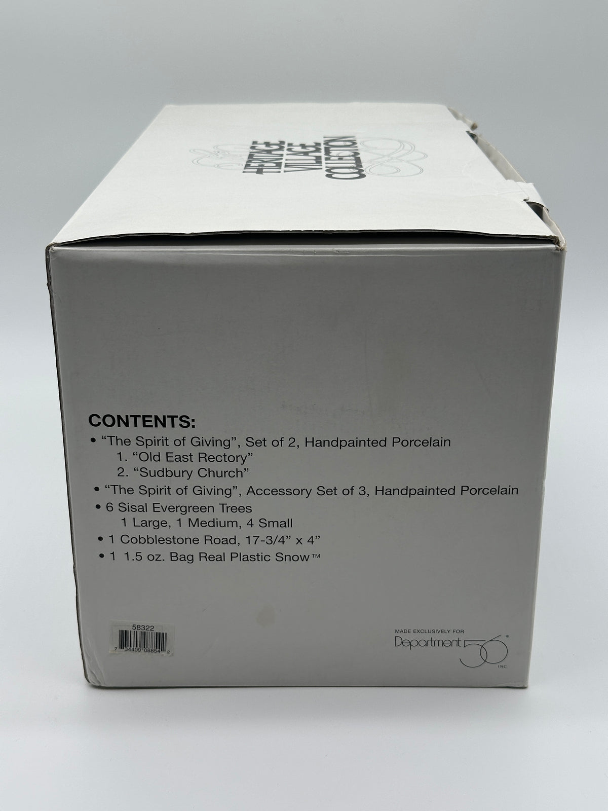 Outer box side listing the contents: two handpainted porcelain buildings, accessory set of 3, six sisal trees, cobblestone road and Real Plastic Snow